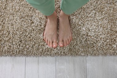 Evdeki yumuşak, açık kahverengi halıda duran kadın, üst manzara.