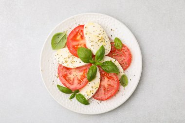 Açık gri masadaki yeşil otlu lezzetli Caprese salatası.