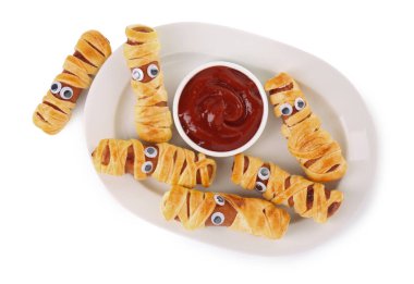 Plate with tasty sausage mummies for Halloween party and ketchup isolated on white, top view clipart