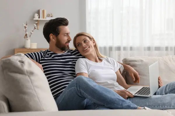 Happy couple with laptop on sofa at home