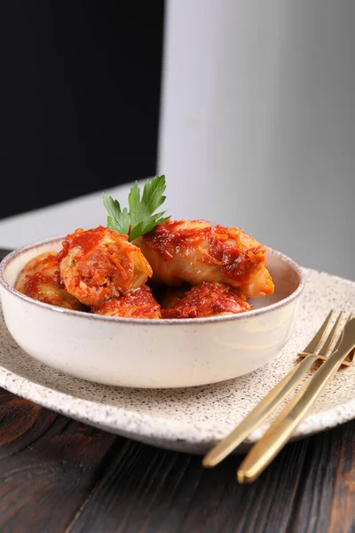 Delicious stuffed cabbage rolls cooked with tomato sauce on wooden table, closeup. Space for text