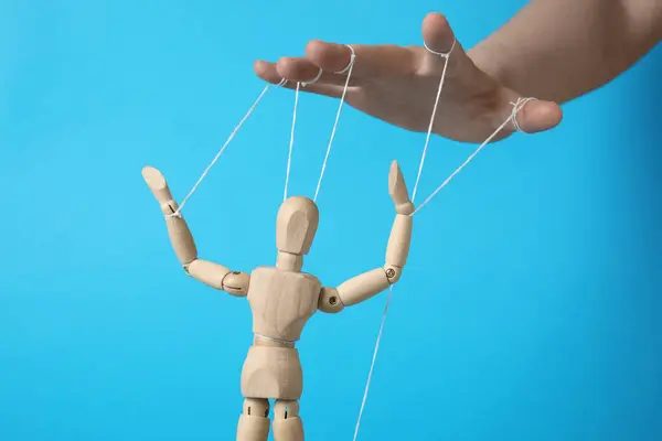 stock image Woman pulling strings of puppet on light blue background, closeup