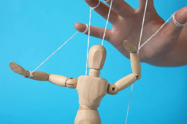 stock image Woman pulling strings of puppet on light blue background, closeup