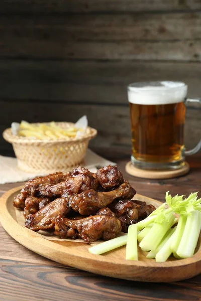 Delicious chicken wings, celery, beer and french fries on wooden table