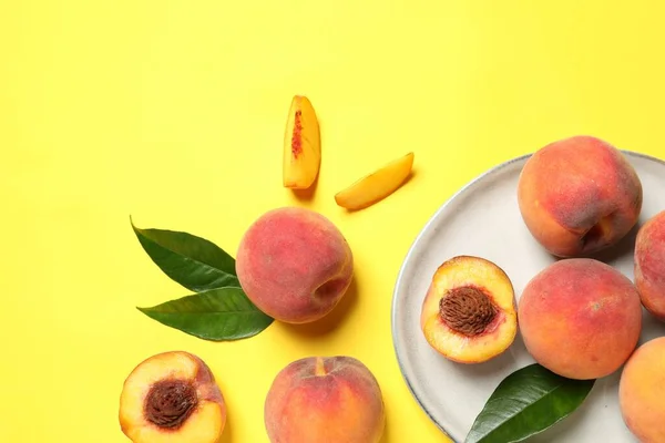 Delicious juicy peaches and green leaves on yellow background, flat lay. Space for text