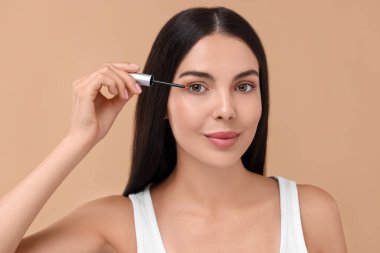 Kirpiklerine bej arka planda serum süren güzel bir kadın. Kozmetik ürünü