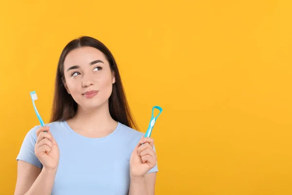Beautiful woman with tongue cleaner and plastic toothbrush on yellow background, space for text