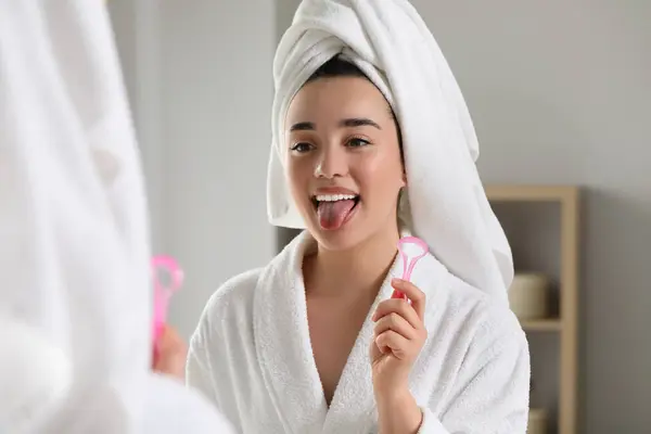 Happy woman with tongue cleaner near mirror in bathroom