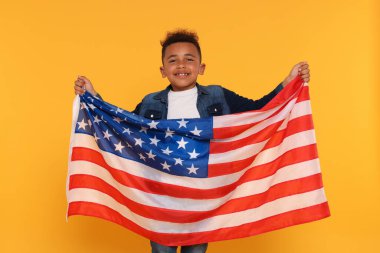 4 Temmuz - ABD 'nin Bağımsızlık Günü. Sarı arka planda Amerikan bayrağı taşıyan mutlu çocuk.