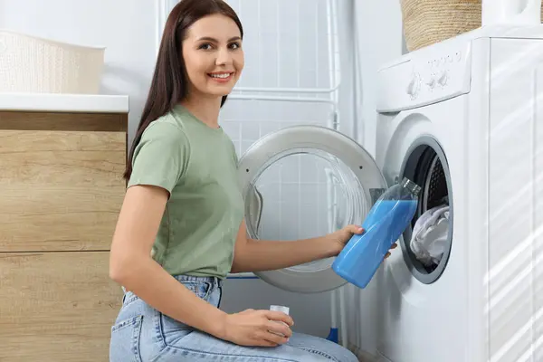 Woman pouring fabric softener into washing machine in bathroom