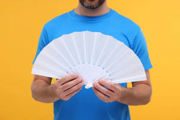 Man holding hand fan on orange background, closeup
