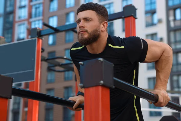 Man training on parallel bars at outdoor gym, low angle view