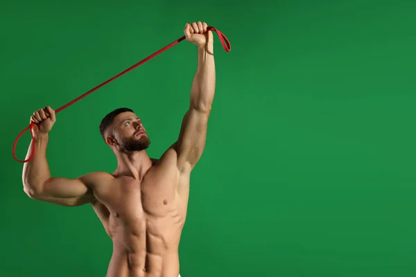 肌肉男在绿色背景上带着弹性阻力带进行运动 案文的篇幅 — 图库照片