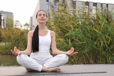 Güzel bir genç kadın yoga minderinde Padmasana egzersizi yapıyor. Lotus pozu