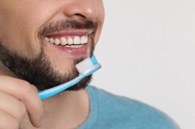 Adam beyaz arka planda plastik diş fırçasıyla dişlerini fırçalıyor, yakın plan. Metin için boşluk