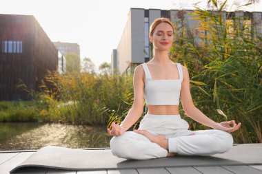 Güzel genç bir kadın yoga minderinde Padmasana egzersizi yapıyor. Lotus pozu