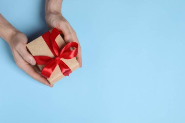 Man holding gift box with red bow on light blue background, top view. Space for text clipart