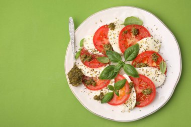 Yeşil masa üzerinde pesto soslu lezzetli Caprese salatası ve kaşık tabağı. Metin için boşluk