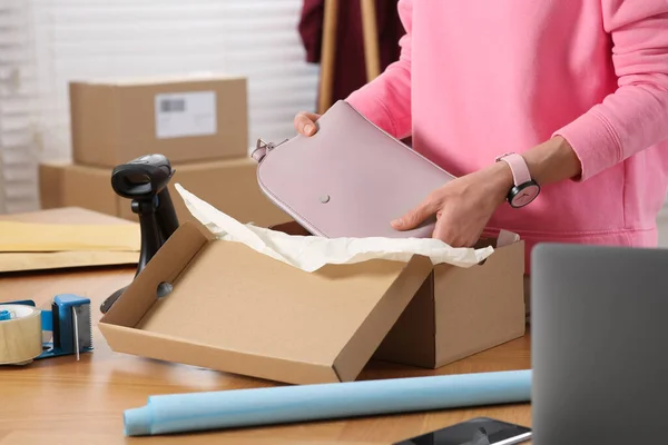 Seller packing bag into cardboard box at table in office, closeup. Online store