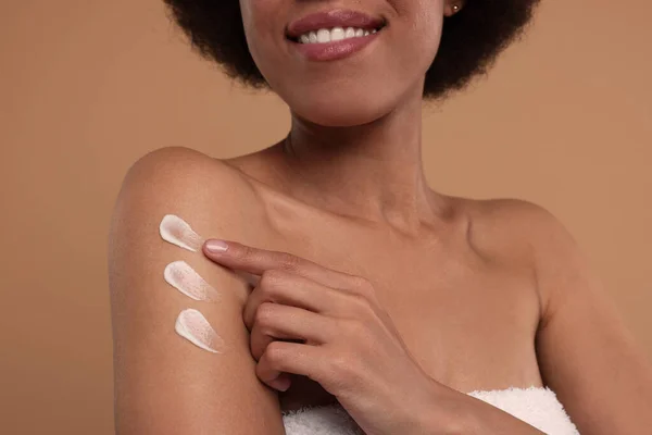 Young woman applying body cream onto arm on beige background, closeup