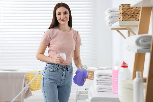 Woman holding fabric softener near washing machine in bathroom