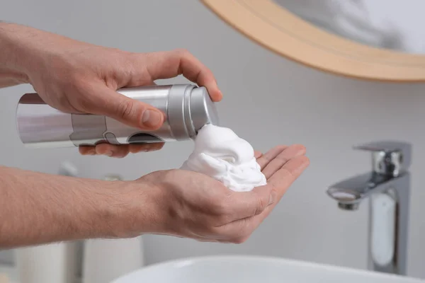 Man applying shaving foam onto hand in bathroom, closeup