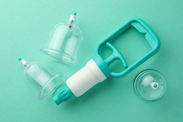 Пластиковые чашки и ручной насос на бирюзовом фоне, плоская укладка. Терапия