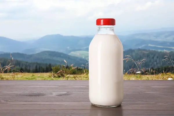 Fresh milk in glass bottle on wooden table against mountain landscape
