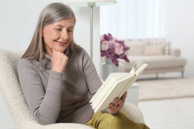 Evdeki koltukta kitap okuyan güzel bir son sınıf öğrencisi.