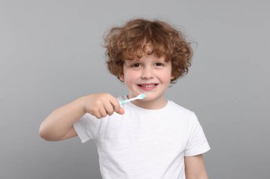 Açık gri arka planda plastik diş fırçası tutan sevimli küçük çocuk.