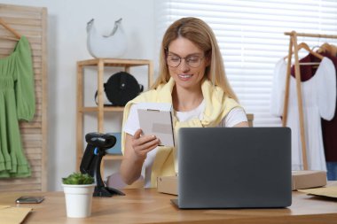 Ofiste çalışan paket ve dizüstü bilgisayarı olan bir satıcı. Çevrimiçi mağaza