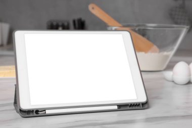 Mutfaktaki beyaz mermer masada boş ekranlı modern tablet, yakın plan.