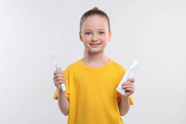 Happy girl holding electric toothbrush and tube of toothpaste on white background