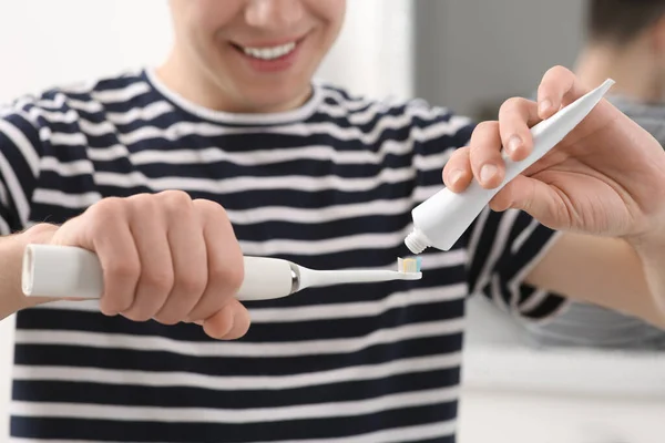 Man squeezing toothpaste from tube onto electric toothbrush in bathroom, closeup