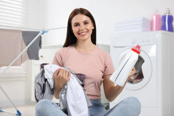 Woman holding fabric softener and dirty clothes in bathroom