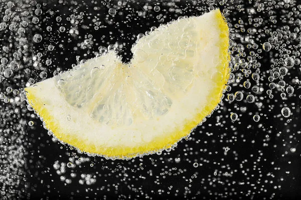 Juicy lemon slice in soda water against black background, closeup