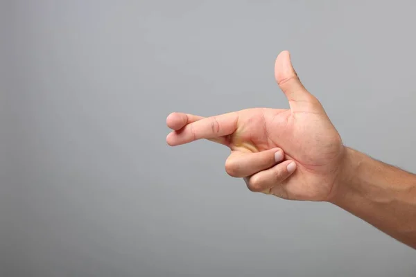 Man crossing his fingers on grey background, closeup. Space for text