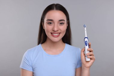 Açık gri arka planda elektrikli diş fırçası tutan mutlu genç kadın.