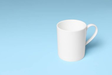 Açık mavi arkaplanda beyaz seramik kupa, metin için boşluk