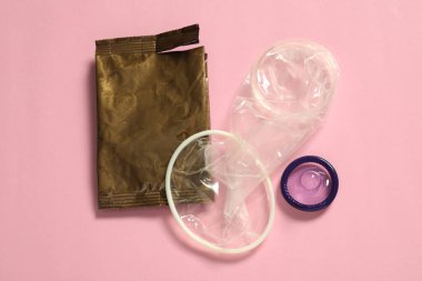 Paketlenmemiş kadın, erkek prezervatifi ve açık pembe arka planda yırtık bir paket. Güvenli seks.