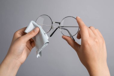 Gri arka planda mikrofiber bezle bardaklarını silen kadın, yakın plan.