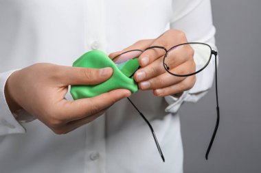 Gri arka planda mikrofiber bezle bardaklarını silen kadın, yakın plan.