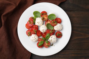 Domatesli Caprese salatası, mozzarella topları ve ahşap masada fesleğen.