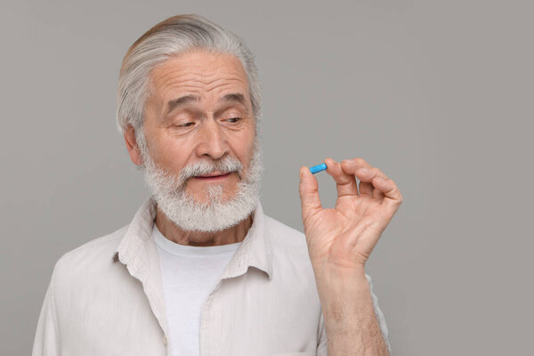 Senior man with pill on grey background