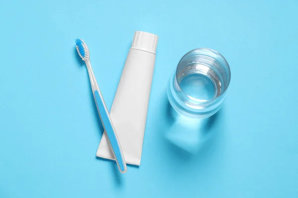 Plastic toothbrush with paste and glass of water on light blue background, flat lay