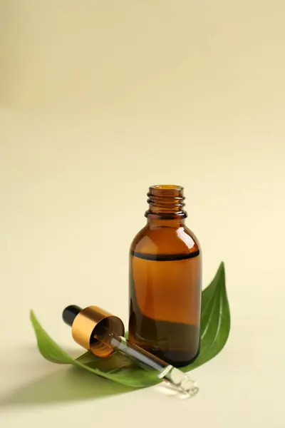 Bottle of cosmetic oil, pipette and leaf on beige background