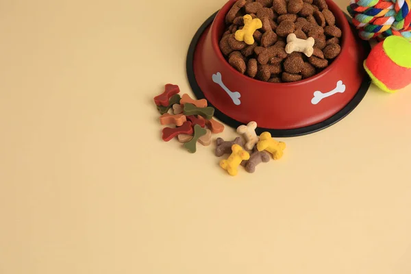 Dry pet food in bowl, vitamins and toys on beige background, above view. Space for text