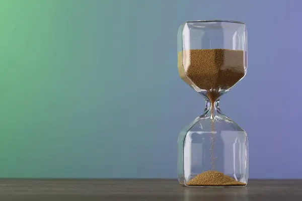 Hourglass with flowing sand on table against color background, space for text