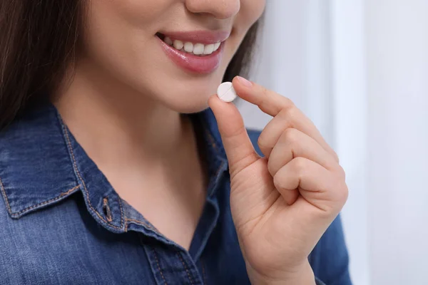 Woman taking pill on blurred background, closeup