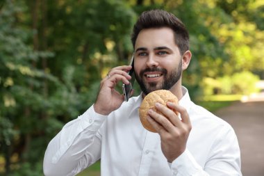 Öğle yemeği vakti. Hamburgerci genç işadamı parkta akıllı telefondan konuşuyor.